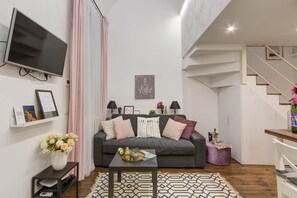 Una sala de estar moderna con un sofá gris, un televisor de pantalla plana, una mesa de centro y una escalera.