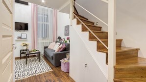 Een moderne woonkamer met een grijze bank, een klein bijzettafeltje en een trap met houten treden.