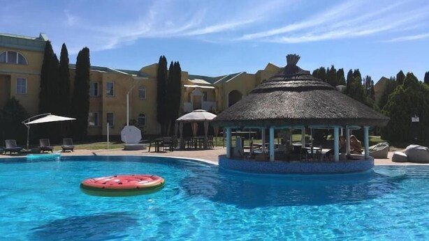 A swimming pool with a thatched gazebo, lounge chairs, and umbrellas. - LB - Art Gallery Apartman (Siófok)