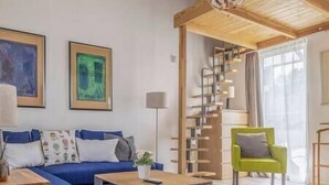 A modern living room with a blue sofa, a green armchair, a wooden coffee table, and a spiral staircase. - LB - Art Gallery Apartman (Siófok)