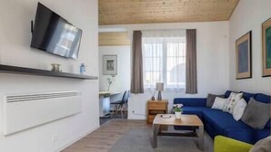 A modern living room with a flat-screen TV mounted on the wall, a blue sofa, a yellow armchair, and a wooden coffee table. - LB - Art Gallery Apartman (Siófok)
