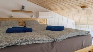 A bedroom with a sloped ceiling, a bed with a patterned blanket, and a small shelf with a plant. - LB - Art Gallery Apartman (Siófok)