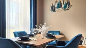 Un coin repas avec une table en bois dressée pour quatre personnes, des chaises bleues et un vase décoratif contenant des fleurs blanches.