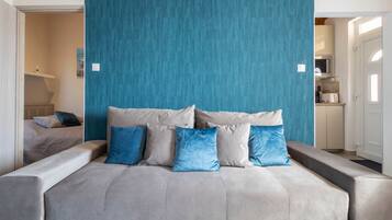 Quarto moderno com uma cama grande, parede de destaque verde-água e uma kitchenette ao fundo.