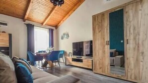 Un salon moderne avec un plafond en bois, un canapé, un coin repas avec des chaises et un téléviseur.