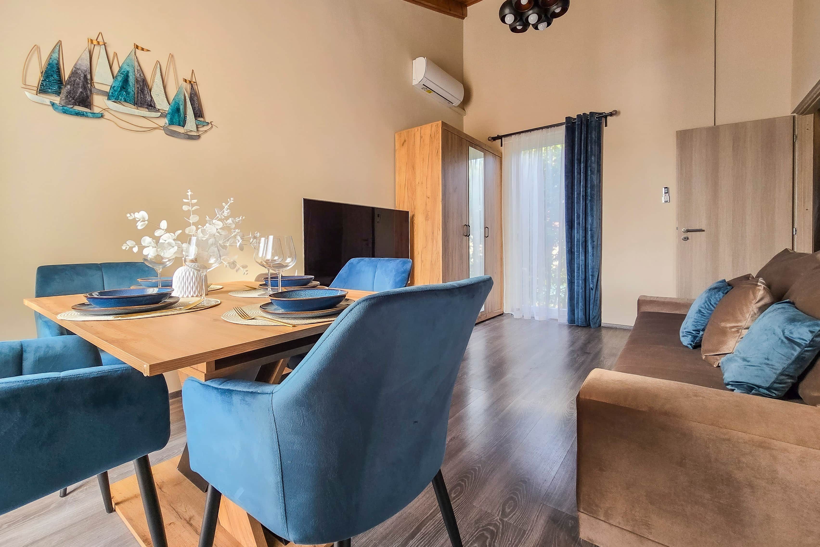 A modern dining area with a wooden table set for four, blue upholstered chairs, and a decorative wall piece.