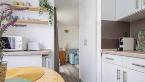 A modern kitchen with white cabinets, a microwave, and a coffee maker. There is a wooden bench with a woven cushion, and a plant in a vase. - LB - MSpirit Apartman Siófok (Siófok)