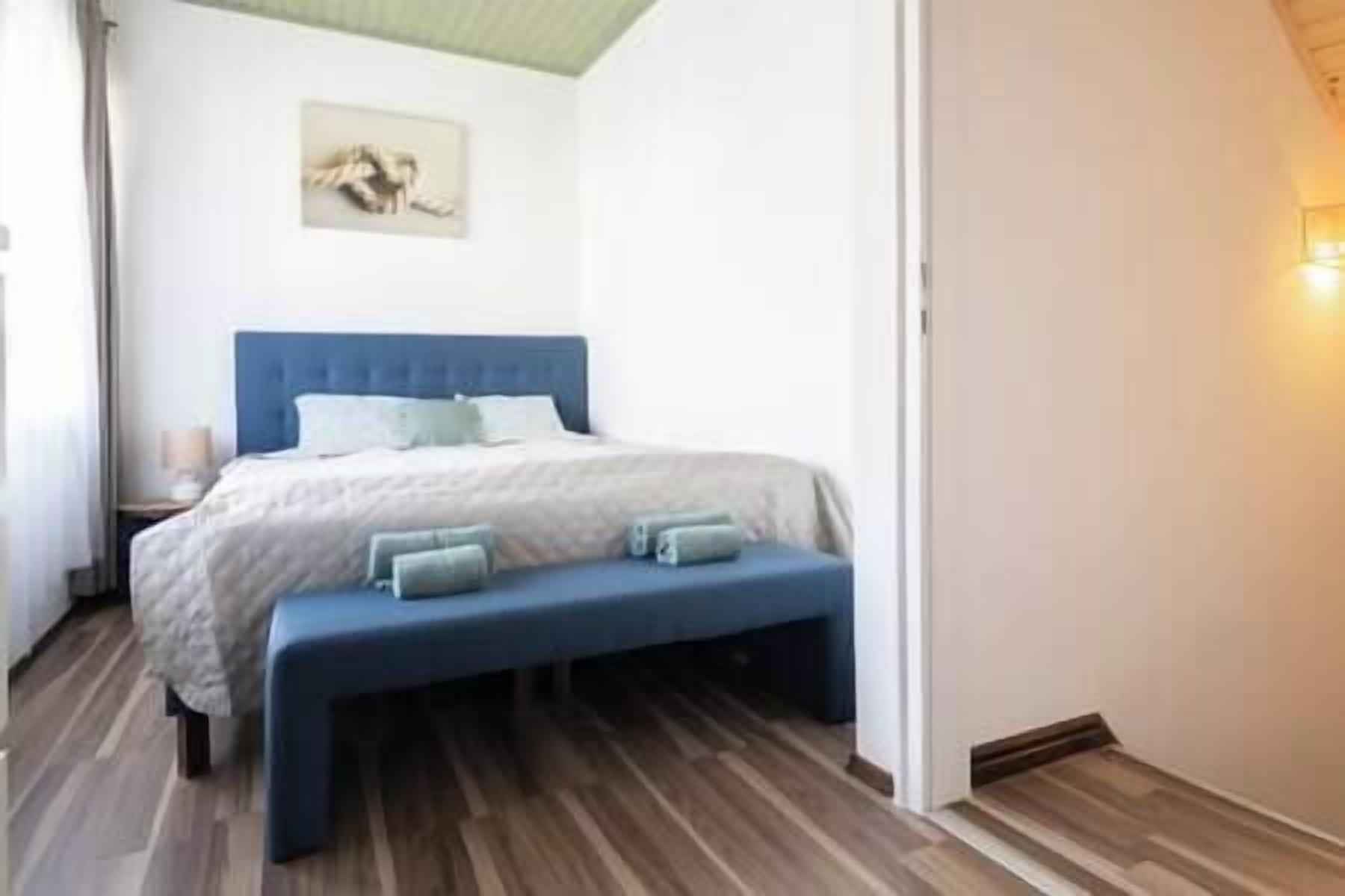 Ein Schlafzimmer mit einem Bett, einer Bank, einem Nachttisch und einem Wandbild.