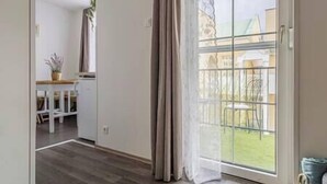 A room with a large sliding glass door leading to a balcony with a view of a grassy area and buildings. - LB - MSpirit Apartman Siófok (Siófok)