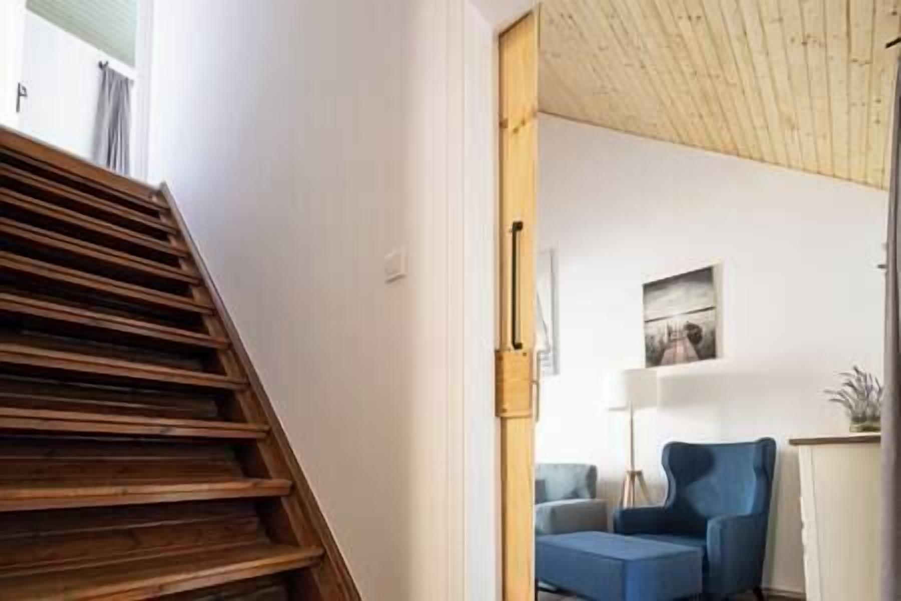 A staircase leading to a room with a blue chair and a painting on the wall.
