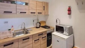 A compact kitchen with wooden cabinets, a sink, a kettle, a microwave, and a small refrigerator. - IMCT - Astoria Apartment Budapest (Budapest)