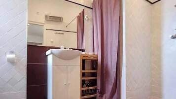A bathroom with a white sink, a mirror, and a wooden shelf.