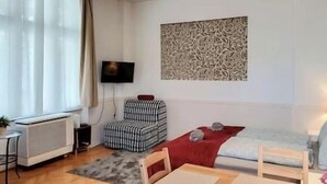 A compact living space with a sofa, a chair, a small table, a radiator, a TV, and a patterned wall decoration. - IMCT - Astoria Apartment Budapest (Budapest)