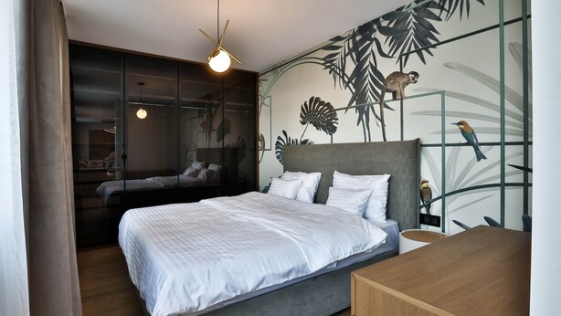 Un dormitorio con cama, escritorio y un mural con motivos naturales.