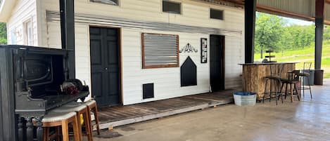 A covered outdoor area with a barbecue grill, wooden tables, and chairs.