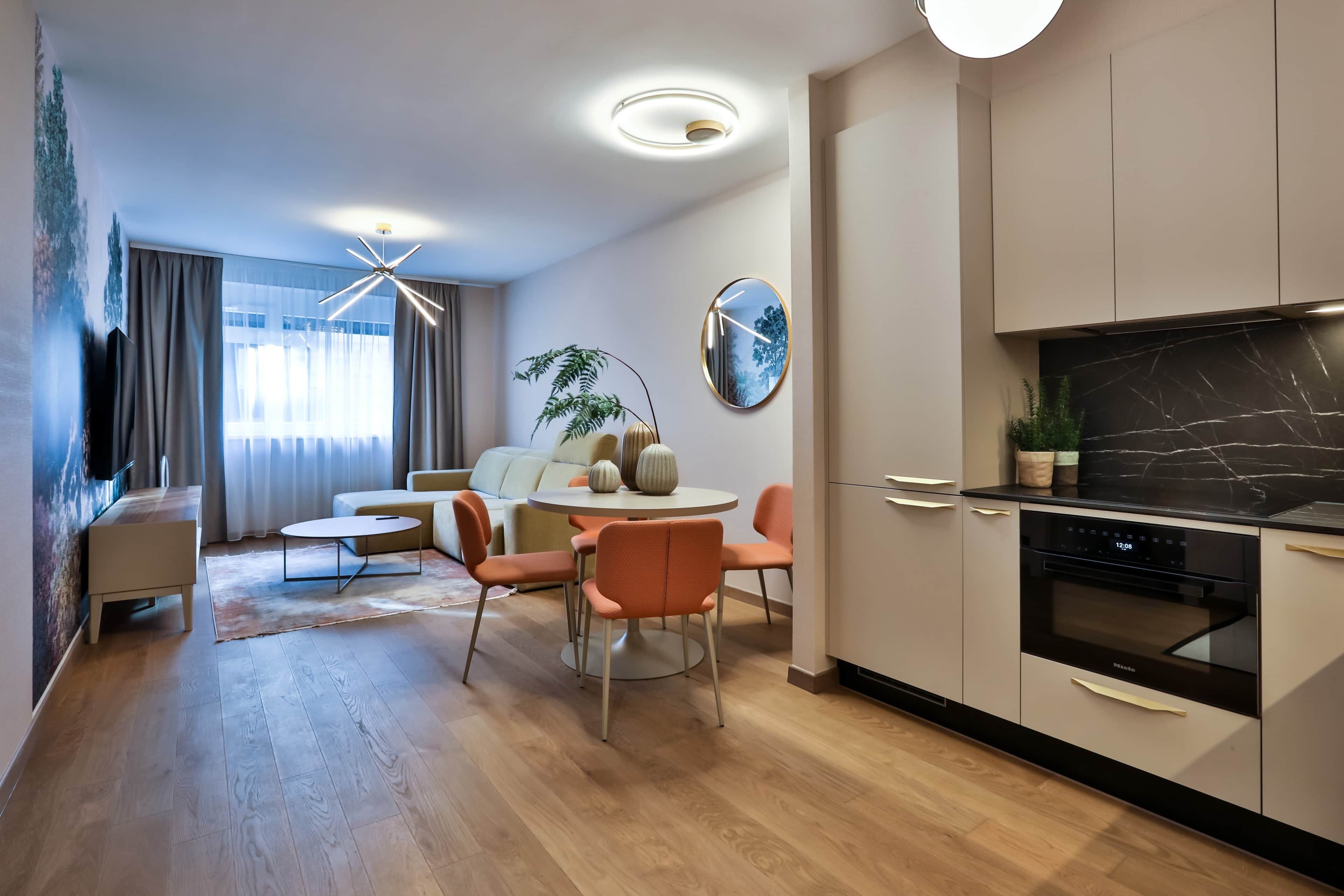 Ein modernes Wohnzimmer mit Essbereich, einer Küche mit schwarzer Arbeitsplatte und einem großen Spiegel an der Wand.