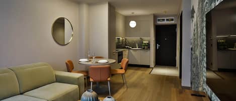 A modern living room with a sofa, a dining table set for two, and a kitchen in the background.