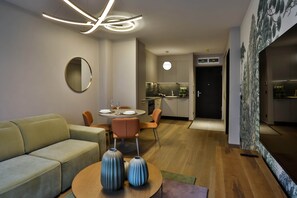A modern living room with a sofa, a dining table set for two, and a kitchen in the background.