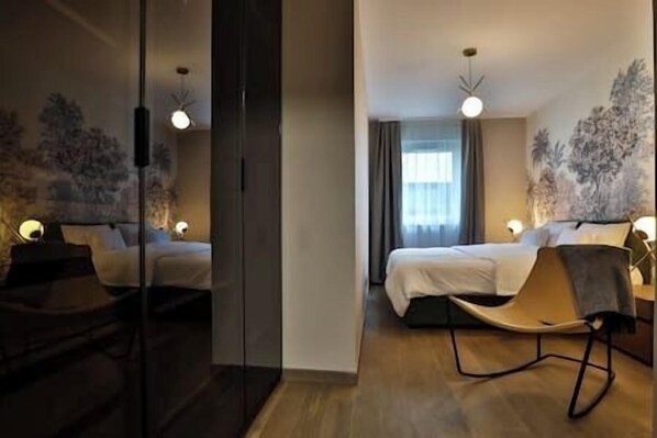A modern hotel room with two beds, a seating area, and a large window.