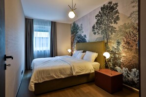 A hotel room with a bed, a nightstand, a wall mural, and a window with curtains.