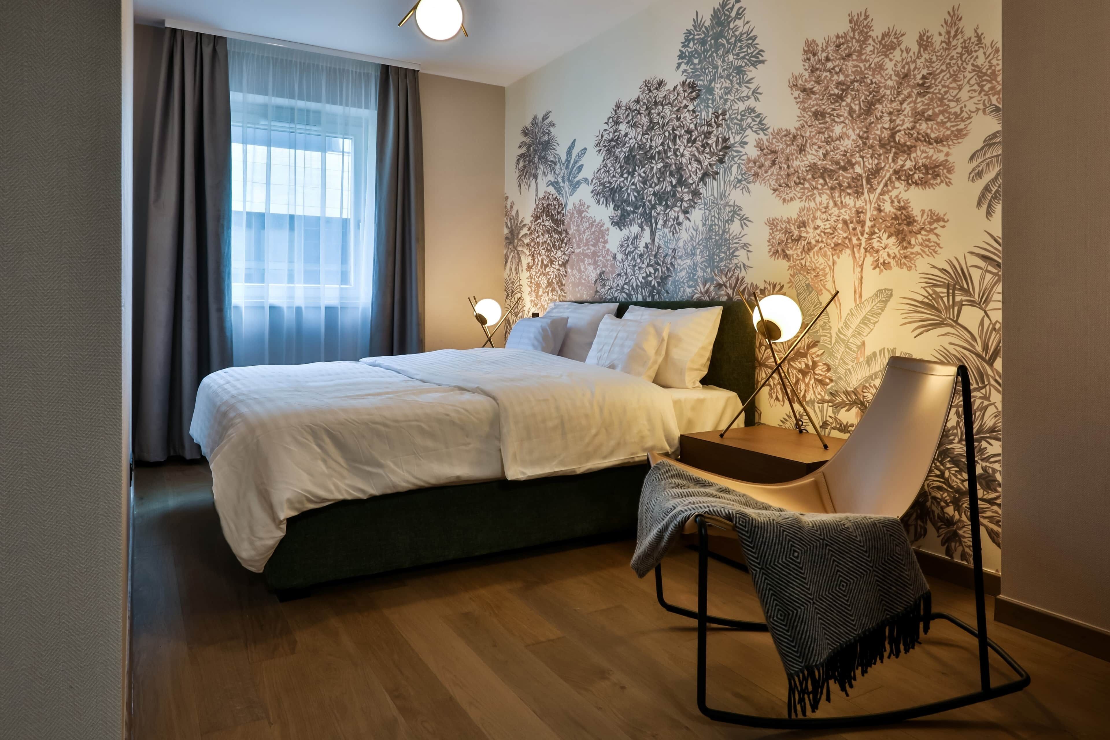 Ein Schlafzimmer mit einem Bett, einem Sessel, einem Nachttisch und einer Wand mit einer Baummalerei.