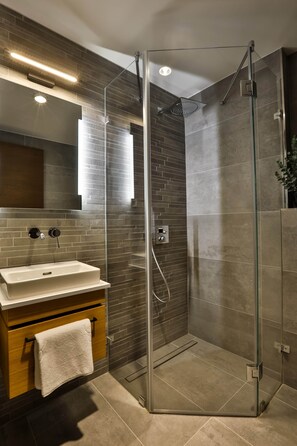 A modern bathroom with a glass-enclosed shower, a vanity with a sink, and a mirror above the vanity. - Sun Hill A201 Luxury Suites (Budapest)