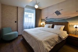 A hotel room with a large bed, a chair, a nightstand with a lamp, and a mural of birds on the wall.
