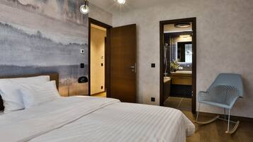 A hotel room with a large bed, a wooden door, a bathroom with a mirror, and a blue chair.
