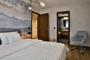 A hotel room with a large bed, a wooden door, a bathroom with a mirror, and a blue chair. - IMCT - Sun Hill A201 Luxury Suites (Budapest)