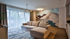A modern living room with a sofa, a dining table with chairs, a large window with sheer curtains, and a wall mural.