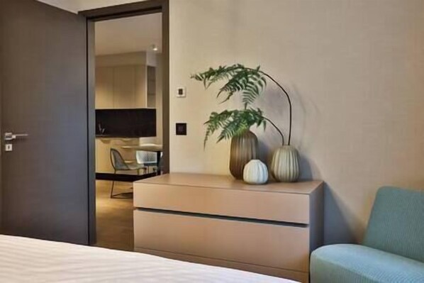 A hotel room with a bed, a dresser, a plant, and a television in the background. - IMCT - Sun Hill A208 Luxury Suites (Budapest)