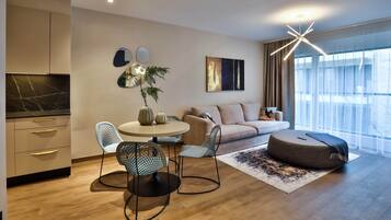 En moderne stue med spiseområde, sofaarrangement, sofabord og et stort vindue med gardiner.