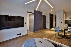 A modern living room with a flat-screen TV, a sofa, and a dining area with chairs and a table. - IMCT - Sun Hill A208 Luxury Suites (Budapest)