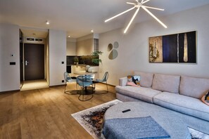 A modern living room with a sofa, a dining area with chairs, a kitchen in the background, and a contemporary light fixture. - IMCT - Sun Hill A208 Luxury Suites (Budapest)