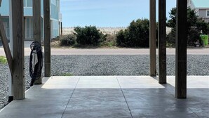 A covered outdoor area with a view of the beach, featuring a concrete floor and wooden pillars.