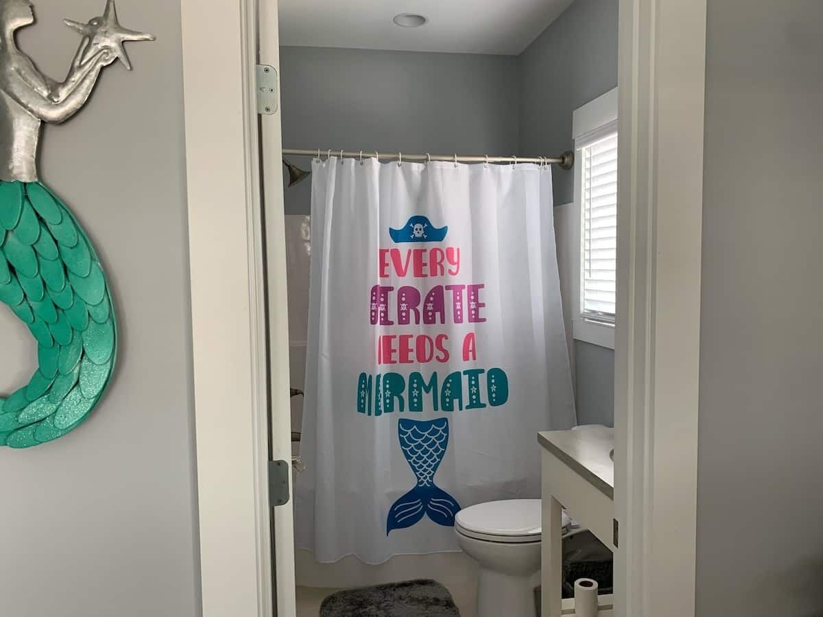 A bathroom with a shower curtain featuring a pirate and mermaid design, a toilet, and a sink.
