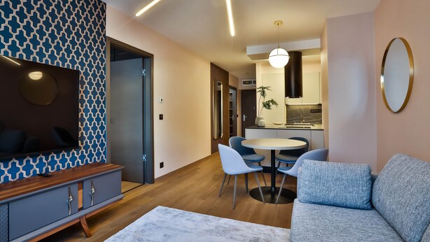 A modern living room with a sofa, a dining table with chairs, a kitchen area, and a patterned wall.