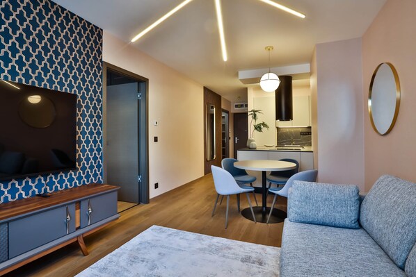 A modern living room with a sofa, a dining table with chairs, a kitchen area, and a patterned wall.