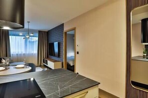 A hotel room with a marble dining table, a bed with a headboard, a large mirror, and a window with curtains. - IMCT - Sun Hill A307 Luxury Suites (Budapest)