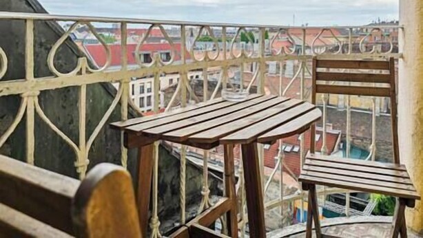 A balcony with a wooden table and chair, overlooking a cityscape. - X - Centrum Charm Apartment (Budapest)