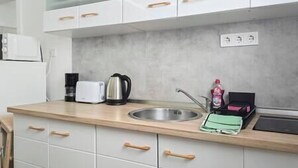 A kitchen with white cabinets, a stainless steel sink, a kettle, a toaster, and a green dish rack. - X - Centrum Charm Apartment (Budapest)