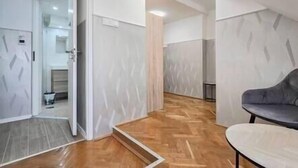 A modern interior with a wooden floor, a grey sofa, and a door leading to another room. - X - Centrum Charm Apartment (Budapest)