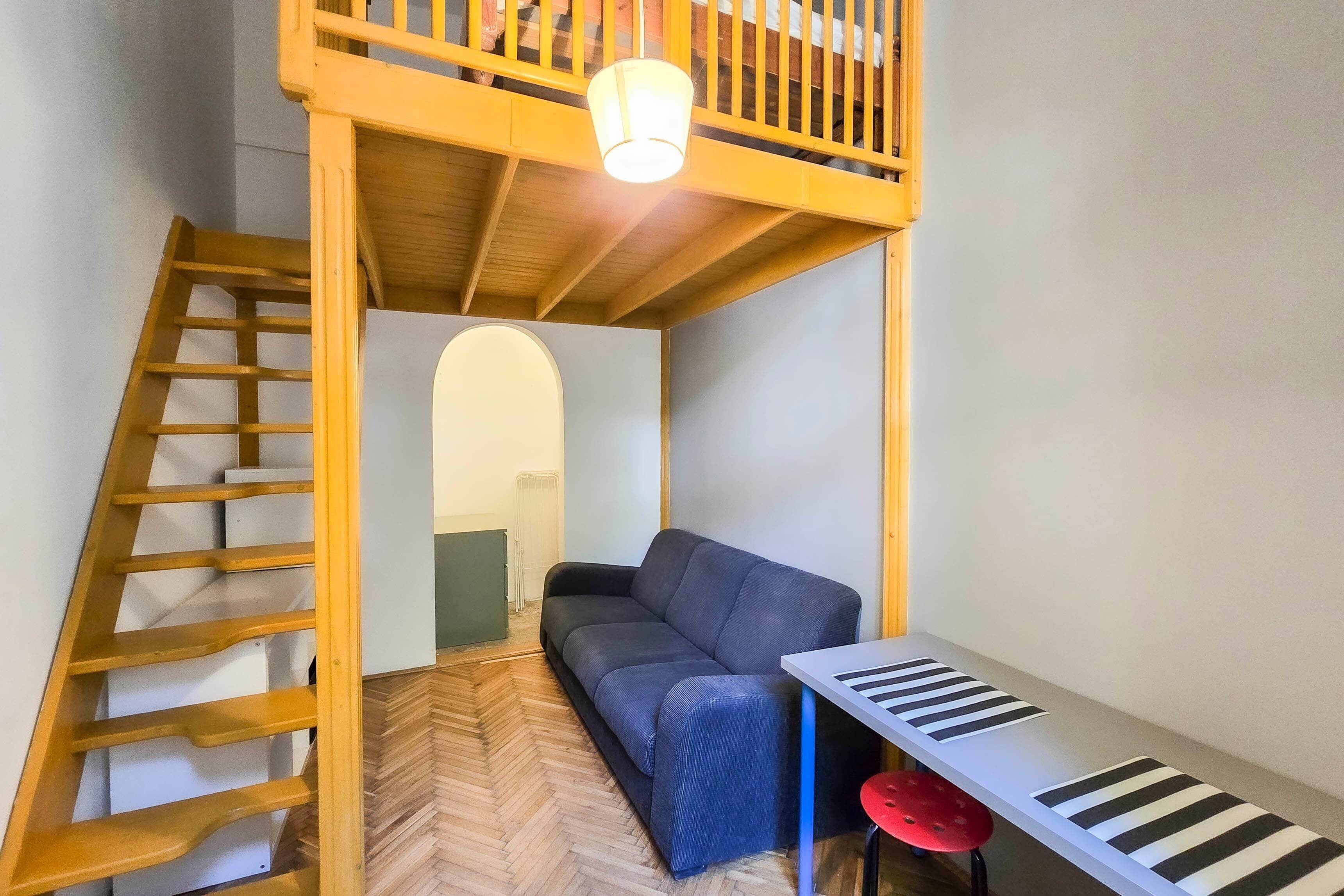 Une pièce avec un lit superposé, un canapé, une petite table avec un clavier et un tabouret rouge.