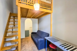 A room with a bunk bed, a sofa, a small table with a keyboard, and a red stool. - IMCT - Seventh Sense Apartment (Budapest)