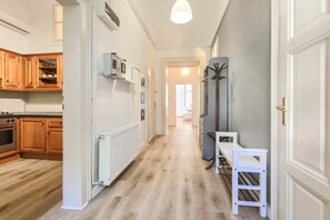 A hallway with a kitchen on the left, a radiator, and a coat rack on the right. - Seventh Sense Apartment (Budapest)