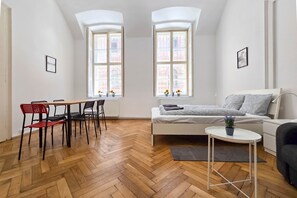 A modern apartment with a herringbone wooden floor, a white sofa, a small round table, and two windows with a view of a brick building. - Seventh Sense Apartment (Budapest)