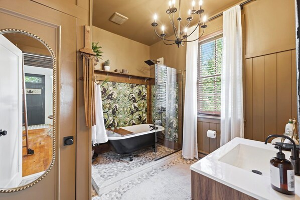 A bathroom with a bathtub, a large mirror, a chandelier, and a window with curtains.