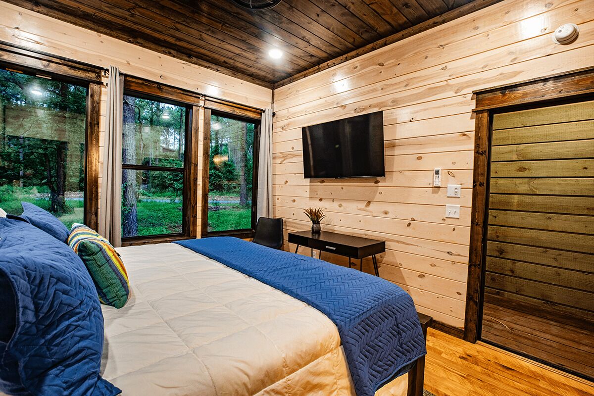 Un dormitorio con una cama, un televisor montado en la pared y una ventana con vistas a zonas verdes.