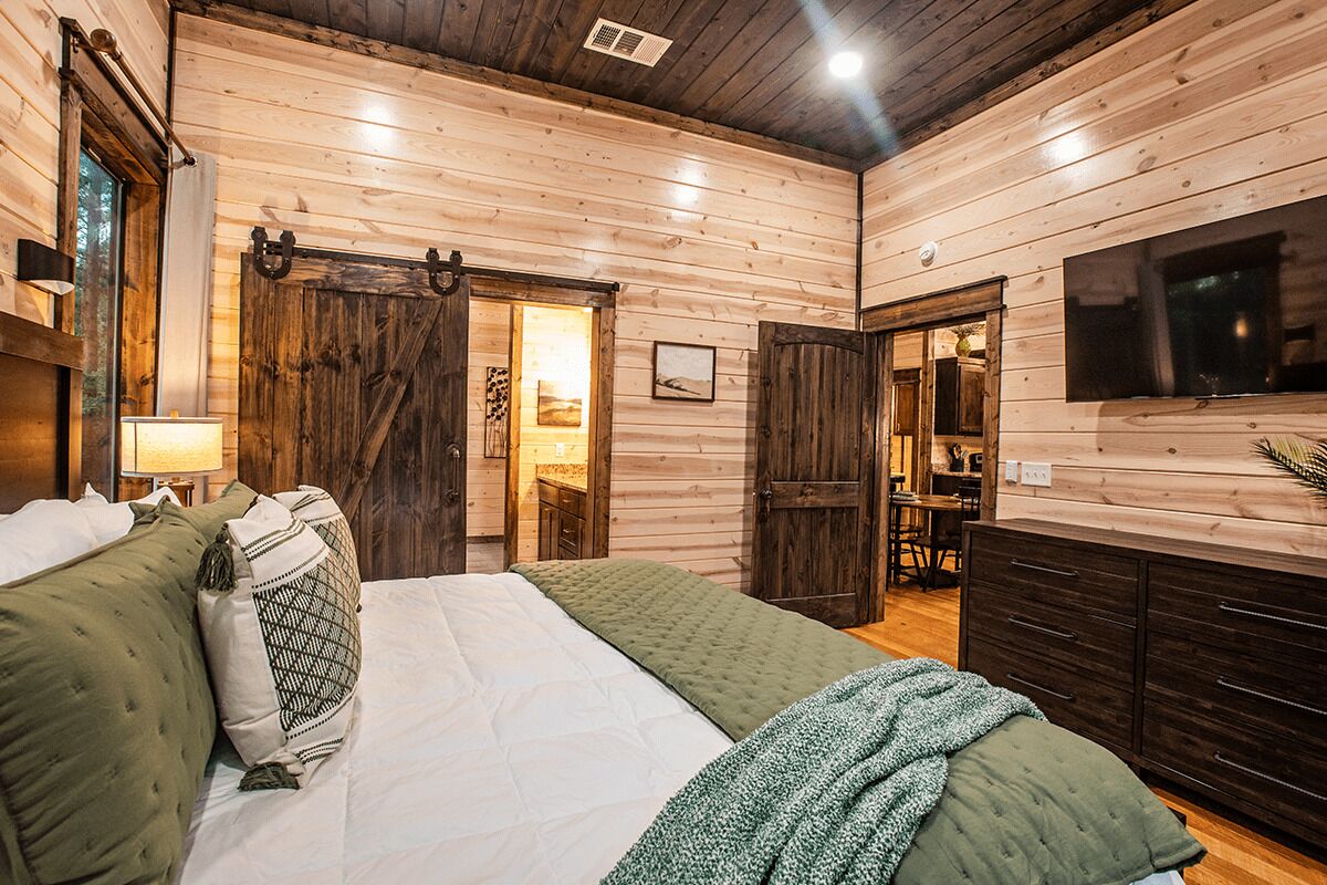 A wooden cabin-style bedroom with a bed, pillows, a dresser, and a television mounted on the wall.