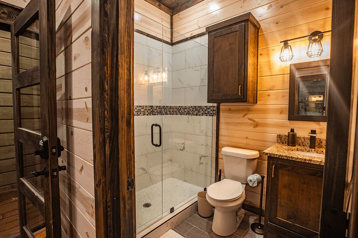A bathroom with a glass-enclosed shower, a toilet, and wooden cabinetry.